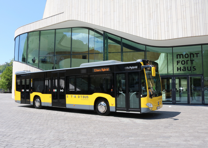 Ein gelber Mercedes eCitaro Elektrobus vom VVV steht vor einem gläsernen Haus.
