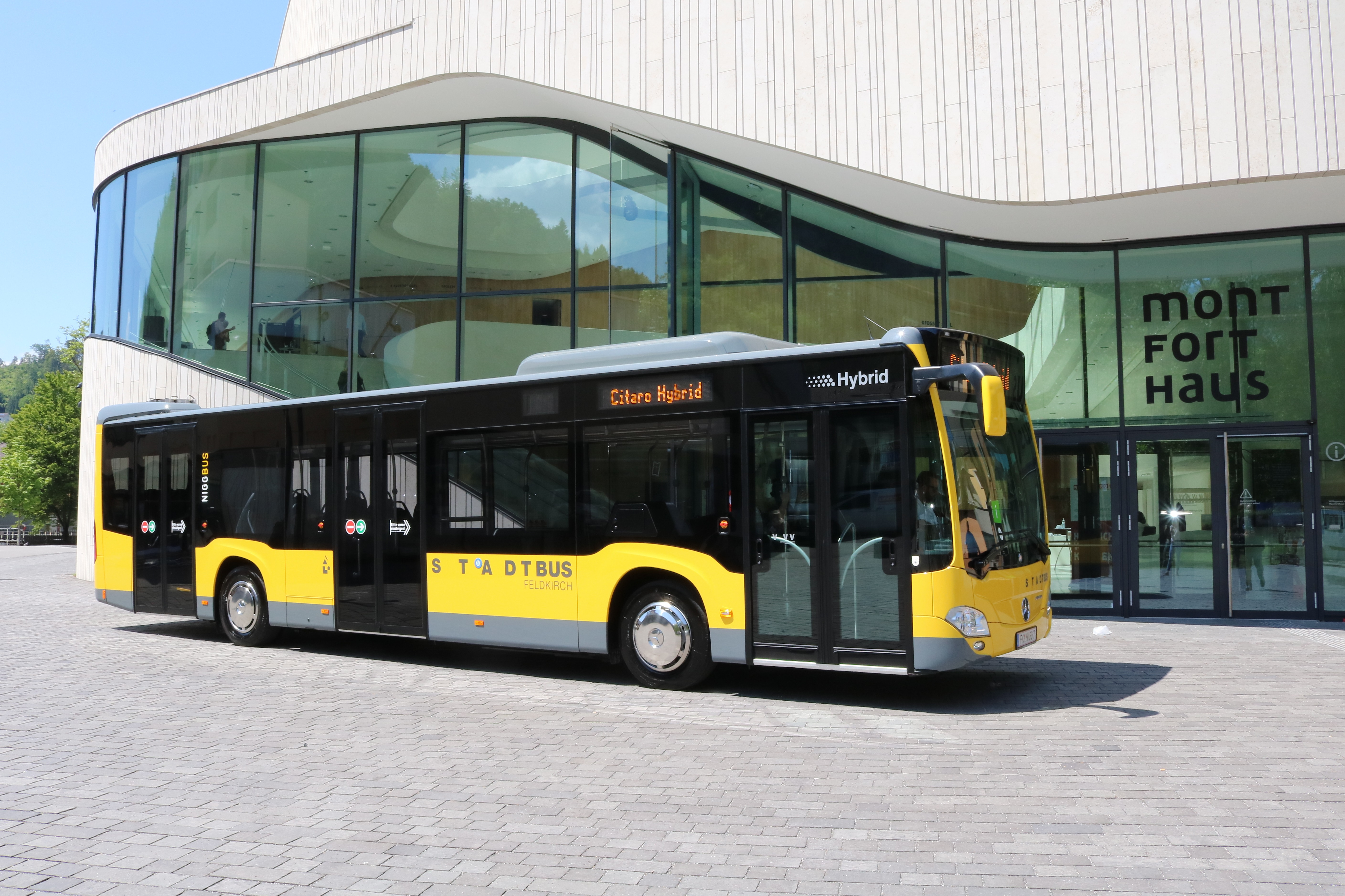 Ein gelber Mercedes eCitaro Elektrobus vom VVV steht vor einem gläsernen Haus.