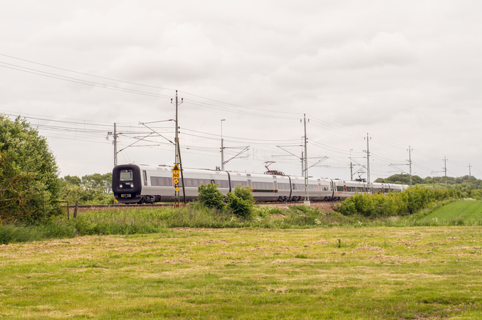 Ein silberner Zug fährt durch grüne Felder.