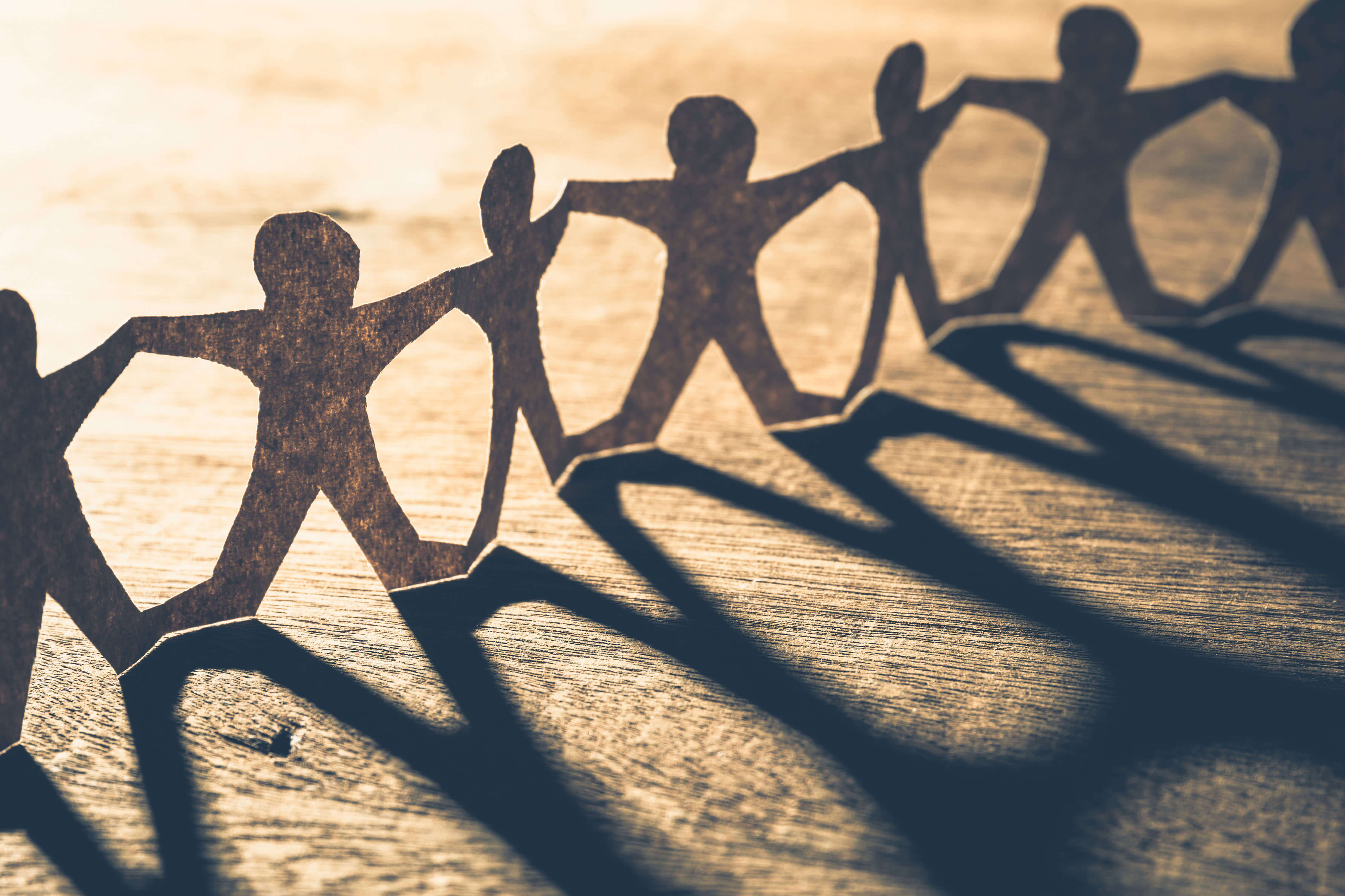 Figuras humanas recortadas de papel en fila cogidas de la mano